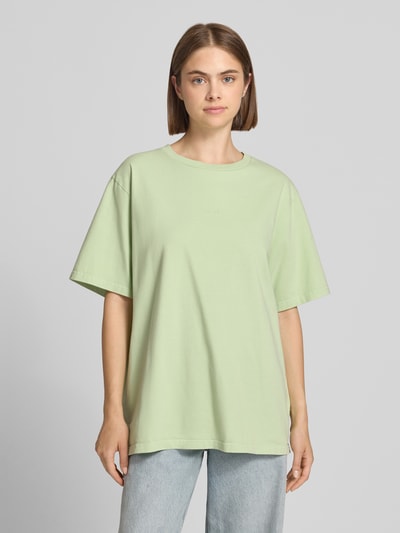 Frauenmodel trägt Oversized T-Shirt mit rückseitigem Print Modell 'Midsummer' von OH APRIL in Hellgrün aus reiner Baumwolle, Ganzkörperansicht von vorne.