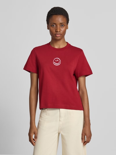 Vrouwenmodel draagt Boxy Fit t-shirt uit pure katoen model 'SARA' van VERO MODA in rood met witte print, vooraanzicht bovenlichaam