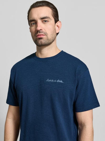 Männermodel trägt T-Shirt mit Label-Stitching von Scotch & Soda in Dunkelblau aus reiner Baumwolle, Regular-Fit, Rundhalsausschnitt, Nahaufnahme Oberkörper.