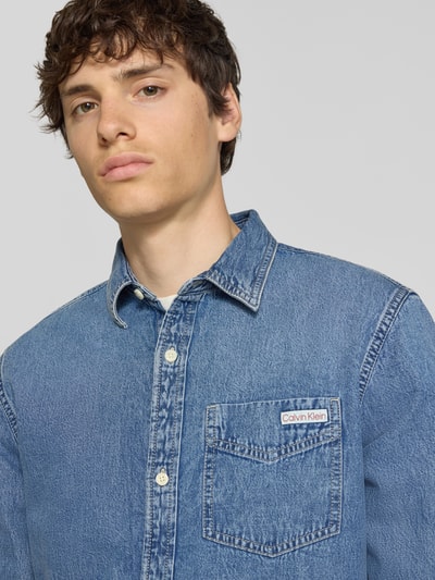 Mannelijk model draagt Regular Fit jeanshemd uit puur katoen van Calvin Klein Jeans in denimlook met labelpatch, borstzak, kentkraag, knoopsluiting, lange mouw, nahaufnahme bovenlichaam.