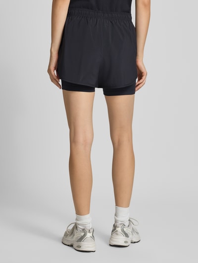 Frauenmodel trägt Shorts im 2-in-1-Look mit Logo von New Balance, elastischer Bund, schwarz, Regular Fit, Ganzkörperansicht Rückansicht.