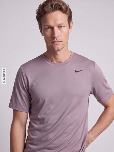 Männermodel trägt T-Shirt mit Logo-Print und Rundhalsausschnitt von NIKE TRAINING in Flieder, glatte Textur, Nahaufnahme Oberkörper, KI-modifiziertes Bild. Rückenlänge bei Größe M: 66 cm, gerader Schnitt.