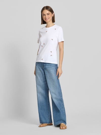 Frauenmodel trägt Regular Fit T-Shirt aus reiner Bio-Baumwolle Modell 'KETTY' von Only, weißes Melange mit Motiv-Stitching, Rundhalsausschnitt, kurzarm, kombiniert mit heller Jeans, Ganzkörperansicht von vorne.