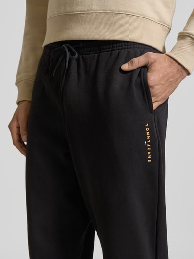Männermodel trägt Regular Fit Sweatpants aus Baumwoll-Mix von Tommy Jeans in Optik: Unifarben mit Label-Stitching-Applikation, Nahaufnahme Hüfte.