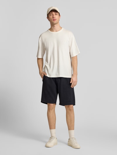 Männermodel trägt Shorts mit elastischem Bund und Logo-Stitching von Pegador aus Baumwoll-Mix, Loose-Fit, schwarze Farbe, Ganzkörperansicht von vorne.