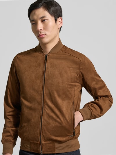 Męski model nosi Bomberjacke in Leder-Optik mit Reißverschlusstaschen od MARKUP, materiał z domieszką stretchu, krój regular fit, kolor brązowy, faktura skóropodobna, kieszenie na zamek, stójka, zamek dwukierunkowy, zdjęcie całej sylwetki z przodu.