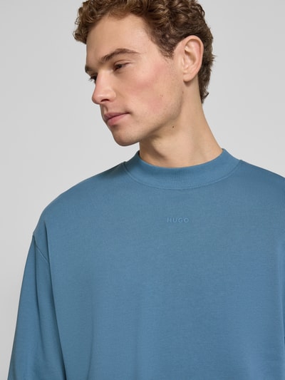 Männermodel trägt Regular Fit Sweatshirt aus reiner Baumwolle Modell 'DAPOCREW' von HUGO in Blau, Rundhals, Label Print, Nahaufnahme Oberkörper.
