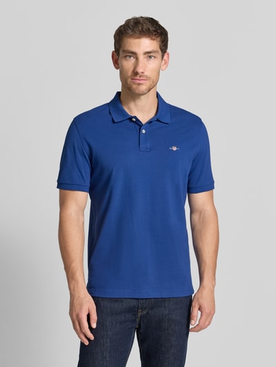 Männermodel trägt Regular Fit Poloshirt aus reiner Baumwolle von GANT in kräftigem Blau mit glatter Textur, Ganzkörperansicht von vorne.