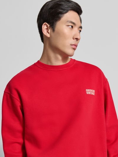 Mężczyzna prezentuje bluzę Sweatshirt mit Logo Modell 'PLIZZY' von American Vintage z czerwonej bawełny, krój relaxed fit, okrągły dekolt, logo, zbliżenie na górną część ciała