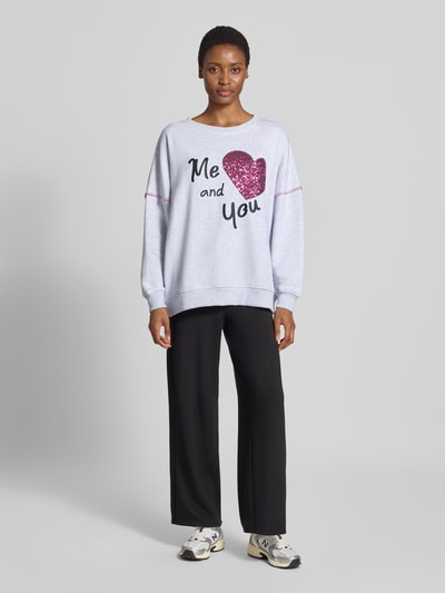 Frauenmodel trägt Oversized Fit Sweatshirt aus reiner Baumwolle von miss goodlife, grau mit Pailettenbesatz, Statement-Print, elastische Abschlüsse, Ganzkörperansicht von vorne.