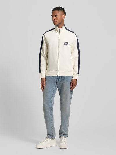 Męski model nosi Sweatjacke mit Zweiwege-Reißverschluss Modell 'FELPA' von ARMANI EXCHANGE, bawełna z domieszką stretchu, krój regular fit, logo na piersi, stojący kołnierz, białe i granatowe kolory, długość tyłu 67 cm, długość rękawa 61 cm, zdjęcie całej sylwetki z przodu.