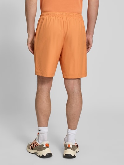 Mannenmodel draagt Relaxed Fit Sport-Shorts met Logo-Stitching van Lacoste Sport, effen oranje met elastische tailleband en zijzakken. Volledige lichaamsopname achteraan.