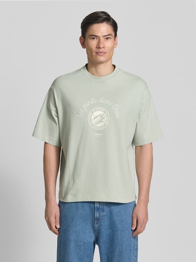 Männermodel trägt Relaxed Fit T-Shirt aus reiner Baumwolle Modell 'BOXYNORMAN GRAPHIC' von SELECTED HOMME, hellgrün, Motiv-Print, Rundhals, Kurzarm, Jersey-Textur, Ganzkörperansicht von vorne