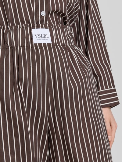 Frauenmodel trägt Weite Hose aus reiner Baumwolle Modell 'MAVIE' von VILLA SOPHIE mit Optik:Allover-Muster, Label-Patch, elastischem Bundabschluss, seitlichen Eingrifftaschen, Regular-Fit, High-Waist, braun mit weißen Streifen, Nahaufnahme Oberkörper.