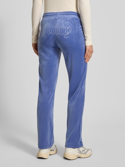 Kobieta prezentuje spodnie dresowe z długimi szwami model 'TINA' od Juicy Couture, mieszanka materiałów z dodatkiem streczu, krój regular fit, elastyczny pas, długość wewnętrzna nogawki 80 cm dla rozmiaru S, widok całej sylwetki od tyłu.
