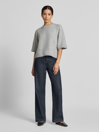 Kobiece modelka nosi szary sweter Oversized Pullover mit Woll-Anteil Modell 'BOOM' od VERO MODA, prosta faktura, ciemne jeansy, pełny widok z przodu