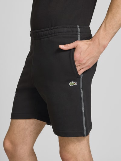 Männermodel trägt Regular Fit Sweatshorts aus reiner Baumwolle von Lacoste, unifarben schwarz, Logostreifen, Label Patch, Nahaufnahme Oberschenkel.