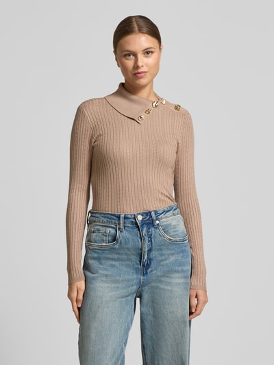 Modelka nosi Slim Fit Longsleeve aus Viskose-Mix Modell 'Sicilla' od Guess w kolorze beżowym, strick-optik, dekoracyjne guziki, krój slim fit, długi rękaw, długość tyłu w rozmiarze S: 52 cm, długość rękawa w rozmiarze S: 61 cm, widok całej sylwetki z przodu.
