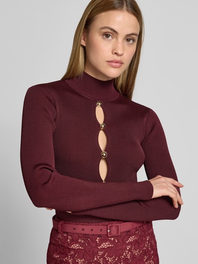 Frauenmodel trägt Slim Fit Longsleeve aus Viskose-Mix von Self-Portrait in Bordeaux, Cut-Outs, Zierbesatz, Rollkragen, Nahaufnahme Oberkörper.