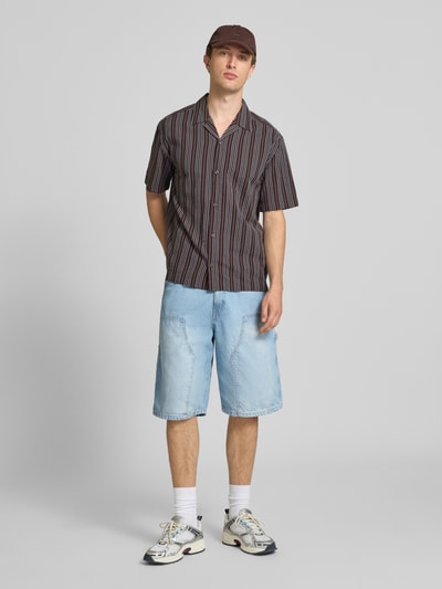 Männermodel trägt Relaxed Fit Freizeithemd aus reiner Baumwolle Modell 'CRUZ' von Only & Sons mit gestreiftem Muster, Resort-Kragen, durchgehender Knopfleiste, Rückenpasse, Ärmelform: Kurzarm, Materialverarbeitung: Seersucker, Farbe: Braun mit Streifen, Ganzkörperansicht von vorne.