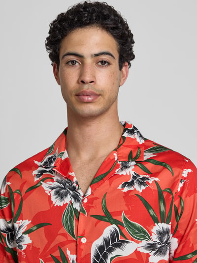Männermodel trägt Regular Fit Freizeithemd mit Reverskragen von Superdry, rotes Muster, grüne und weiße Details, Nahaufnahme Oberkörper. Reine Baumwolle, Modern Fit, Knopfleiste.