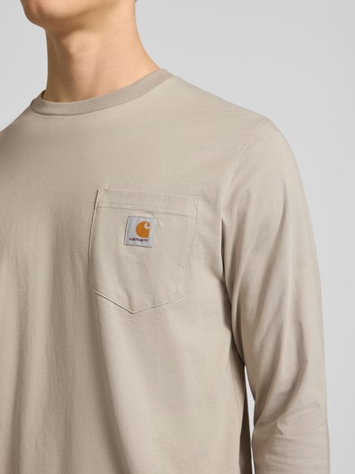 Männermodel trägt Longsleeve mit Brusttasche und Label-Detail von Carhartt Work In Progress aus Baumwolle, Regular Fit, Nahaufnahme Oberkörper.
