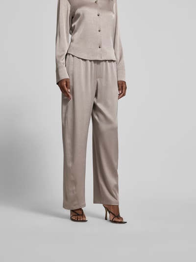 Vrouwenmodel draagt Stoffhose met elastische tailleband van Nanushka in beige fluweel, relaxed fit, siernaden, detailopname onderlichaam.