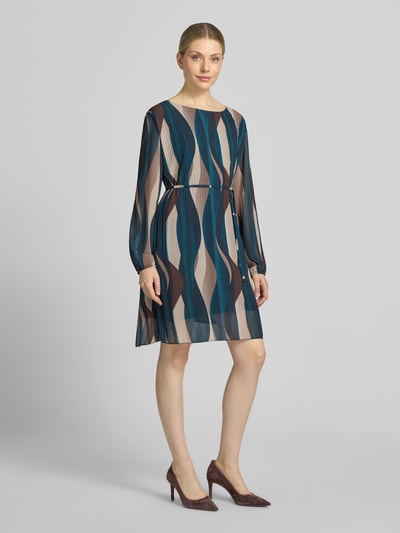 Frauenmodel trägt knielanges Kleid mit Bindegürtel Modell 'Sa44raa' von ZABAIONE aus Chiffon, Allover-Look, Plisseefalten, Rundhalsausschnitt, gemusterte Farben in Blau, Beige und Braun, gerader Schnitt, Ganzkörperansicht von vorne.