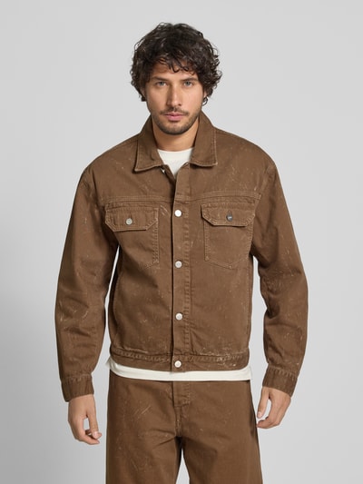 Męski model nosi Jeansjacke mit Brusttaschen Modell 'Type 10' od Wood Wood w brązowym kolorze, krój regular fit, czysta bawełna, tekstura z przetarciami, długość tyłu w rozmiarze M 66 cm, szerokość ramion w rozmiarze M 55 cm, szerokość klatki piersiowej w rozmiarze M 57 cm, długość rękawa w rozmiarze M 64 cm, widok całej sylwetki z przodu.