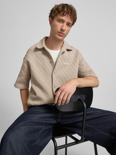 Männermodel trägt Modern Fit Freizeithemd mit Logo-Stitching Modell 'Jovren' von Pegador, Strukturmuster, Kentkragen, Material-Mix, Knopfleiste, Beige und Weiß, Jeans, Nahaufnahme Oberkörper.