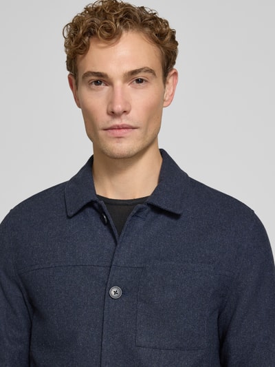 Mężczyzna model nosi Regular Fit Jacke mit Woll-Anteil von Lindbergh, elastyczna mieszanka materiałów z dodatkiem wełny, wykładany kołnierz, kieszeń na piersi, listwa guzikowa, kolor ciemnogranatowy, długość tyłu w rozmiarze M: 72 cm, zbliżenie na górną część ciała