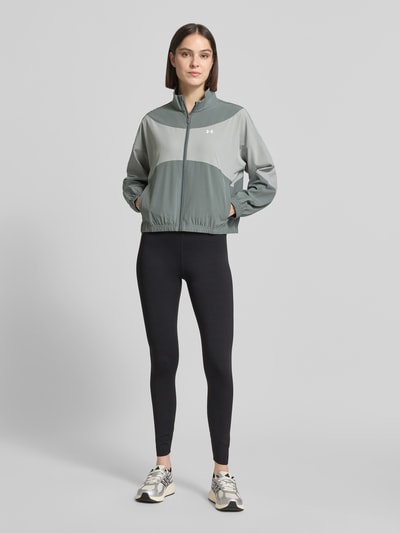 Frauenmodel trägt Trainingsjacke mit Stehkragen und Eingrifftaschen von Under Armour, Regular-Fit, Logo, Reißverschluss, Zweifarbig, mattes Material, Rückenlänge bei Größe S: 60 cm, Schulterbreite: 62 cm, Brustweite: 57 cm, Ärmellänge: 50 cm; Ganzkörperansicht von vorne.