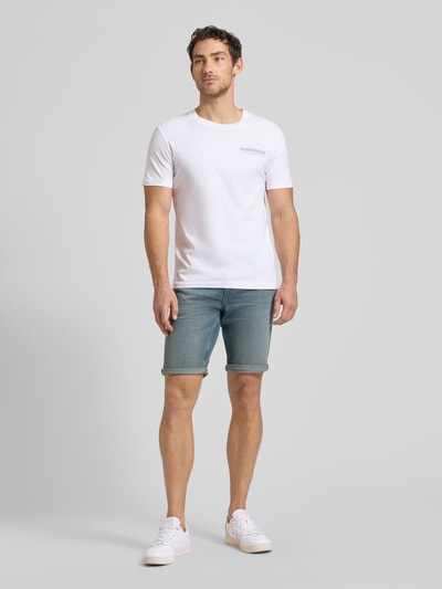 Męski model nosi Regular Fit Jeans Bermudas aus Baumwoll-Mix von Tom Tailor, stylizowana na denim, krój regular fit, mieszanka bawełny, 5 kieszeni, naszywka z logo, szlufki na pasek, zapięcie na guzik i zamek błyskawiczny, jasnoniebieski, gładka tekstura, Ganzkörperansicht von vorne.