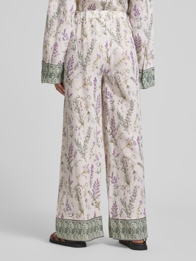 Frauenmodel trägt Wide Leg Leinenhose mit Lavendelprint von Christian Berg Woman, florales Muster in Lila und Grün, elastischer Bund, Ganzkörperansicht Rückansicht.