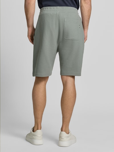 Männermodel trägt Shorts mit Strukturmuster und Tunnelzug von Lerros aus Baumwoll-Mix mit Stretch-Anteil in Grün, Ganzkörperansicht Rückansicht. Regular-Fit, elastischer Bund, Gesäßtasche, Bundweite Größe 38: 49 cm, Innenbeinlänge: 22 cm.