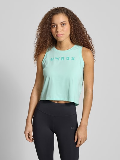 Frauenmodel trägt PUMA x HYROX - Crop Top mit Label-Print von PUMA, mintgrün, Material-Mix mit Stretch-Anteil, Regular-Fit, gerippter Rundhalsausschnitt, Rückenlänge 49 cm bei Größe S, Ganzkörperansicht von vorne.