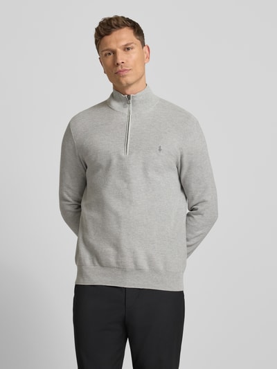 Męski model nosi Sweter z dzianiny z wyhaftowanym logo od Polo Ralph Lauren, bawełna, krój regular fit, prążkowane wykończenia, stójka, krótki zamek błyskawiczny, długość tyłu 70 cm, długość rękawów 68 cm, kolor jasnoszary, gładka faktura, prążki na wykończeniach, całkowity widok z przodu.