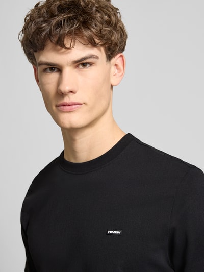 Männermodel trägt Basic T-Shirt mit kleinem Logo-Patch auf der Brust von REVIEW, reine Baumwolle, gerader Schnitt, Nahaufnahme Oberkörper.