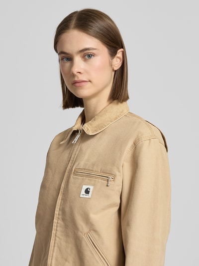 Frauenmodel trägt Jacke mit Label-Detail von Carhartt Work In Progress aus beiger Baumwolle, Reißverschluss, Nahaufnahme Oberkörper.