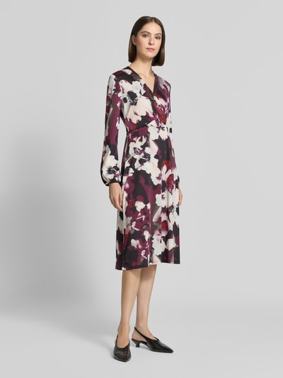 Frauenmodel trägt Midikleid in Wickel-Optik mit V-Ausschnitt von ZABAIONE, florales Muster mit A-Linie, Material-Mix, Ganzkörperansicht von vorne.
