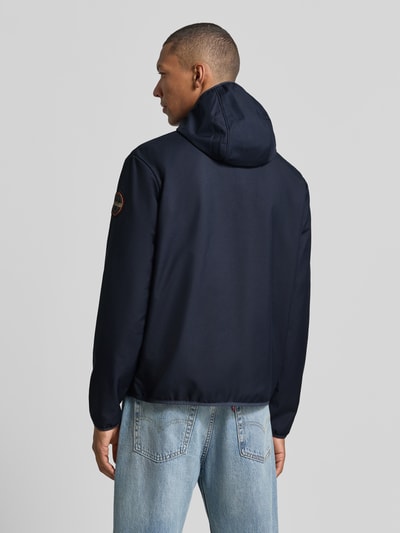 Męski model nosi Regular Fit Jacke mit Logo-Print od Napapijri, granatowa kurtka, stójka, wpuszczane kieszenie, zamek błyskawiczny, elastyczne wykończenia, długość tyłu w rozmiarze M: 69 cm, szerokość ramion: 52 cm, szerokość w rozmiarze M: 60 cm, długość rękawów: 68 cm, widok całej sylwetki z tyłu.