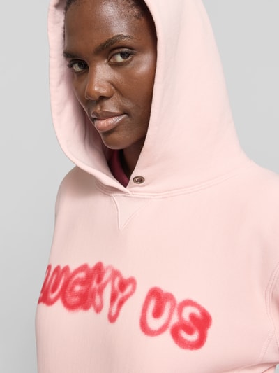 Frauenmodel trägt Oversized Hoodie aus reiner Baumwolle von Kenzo in Rosa mit Statement-Print und Känguru-Tasche, Nahaufnahme Oberkörper. Rückenlänge bei Größe S: 59 cm, elastische Abschlüsse.