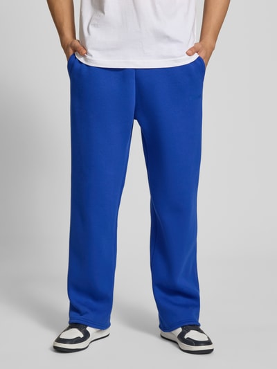 Mannenmodel draagt Sweatpants mit elastischem Bund van REVIEW in felblauw, relaxed fit, materiaalmix met katoen, achterzak, binnenbeenlengte maat M 76 cm. Ganzkörperansicht van voren.