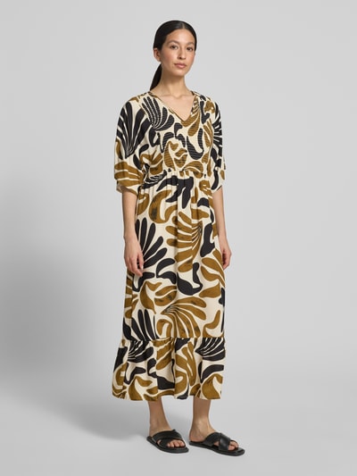 Frauenmodel trägt Midikleid aus Viskose mit Smok-Details Modell 'FELDI' von Soyaconcept, gemusterte Naturtöne, Ganzkörperansicht von vorne, taillierter Schnitt, V-Ausschnitt, reine Viskose, Ärmellänge 25 cm, Rückenlänge 119 cm, Brustweite 44 cm.