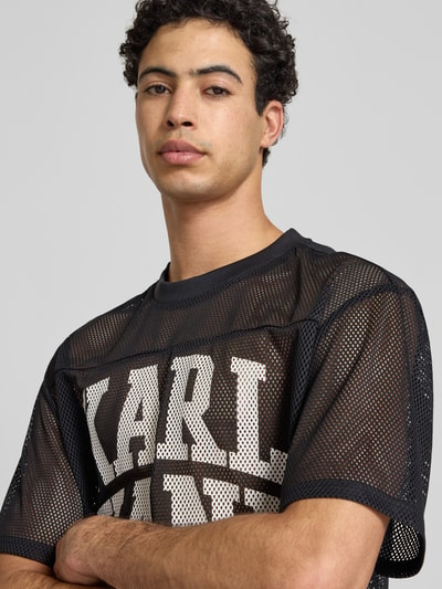 Männermodel trägt Oversized T-Shirt mit Logo-Print von KARL KANI aus schwarzem Mesh, Rundhalsausschnitt, Oversized-Fit, Nahaufnahme Oberkörper.