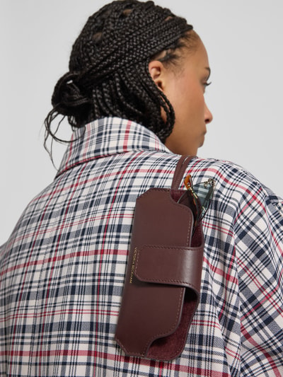 Vrouwenmodel draagt Sonnenbrillenetui aus Leder van Victoria Beckham in bordeaux, met gecoat leer, draagband, overslag, labeldetail en hoofdvak. Ganzkörperansicht Rückansicht.
