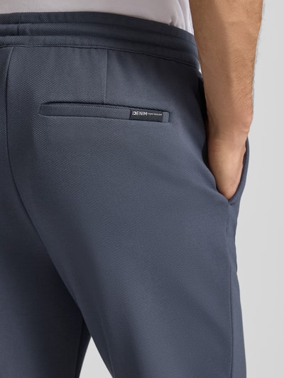 Männermodel trägt Tapered Chino mit Viskose-Anteil von Tom Tailor Denim, Optik: Unifarben, Label-Stitching-Applikation, Nahaufnahme Rückansicht.