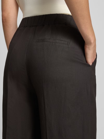 Vrouwenmodel draagt Wide Fit broek uit viscosemix met linnen van Someday, model 'Cisilia', donkerbruin, detailopname achterkant. Context: dames broek van Someday, viscosemix met linnen, wide fit, model 'Cisilia', bandplooien, persplooien, haakjes- en ritssluiting, bandwijdte bij maat 36: 43 cm, binnenbeenlengte bij maat 36: 74 cm.
