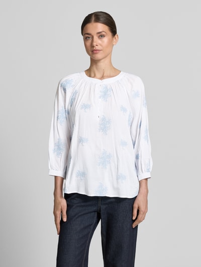 Frauenmodel trägt Bluse aus Viskose-Mix mit verlängertem Rücken von Apricot in Weiß mit hellblauem Muster, Loose-Fit, Rundhalsausschnitt, kurze Knopfleiste, Viskose-Baumwoll-Mix, Rückenlänge 68 cm, Ärmellänge 52 cm, Ganzkörperansicht von vorne.