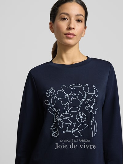 Frauenmodel trägt dunkelblaues Sweatshirt mit weißem Label-Print, lockerer Schnitt, Rundhalsausschnitt, Modell 'BANU' von Soyaconcept, Nahaufnahme Oberkörper.